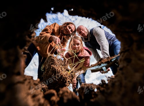 Preview: Low view of smiling family looking at hole for planting tree seedling.