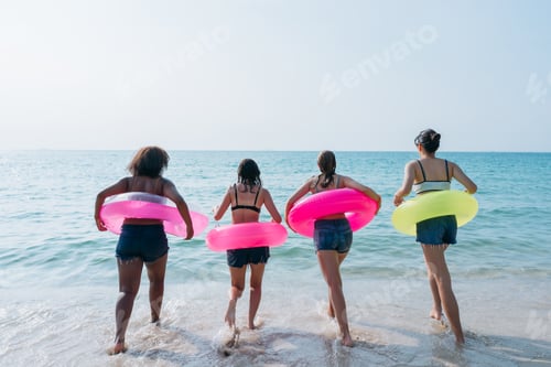 Preview: Teenagers laughing and playing in the sea with colorful swim rings, enjoying youthful summer fun.