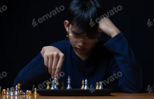 Preview: Young boy playing chess board between golden team and silver team ,he thinking serious how to winner