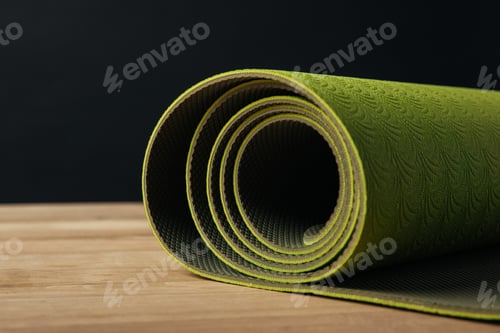 Preview: green rolled yoga mat on wooden tabletop on black