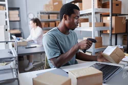 Preview: Young male worker of storage room scanning code on packed box