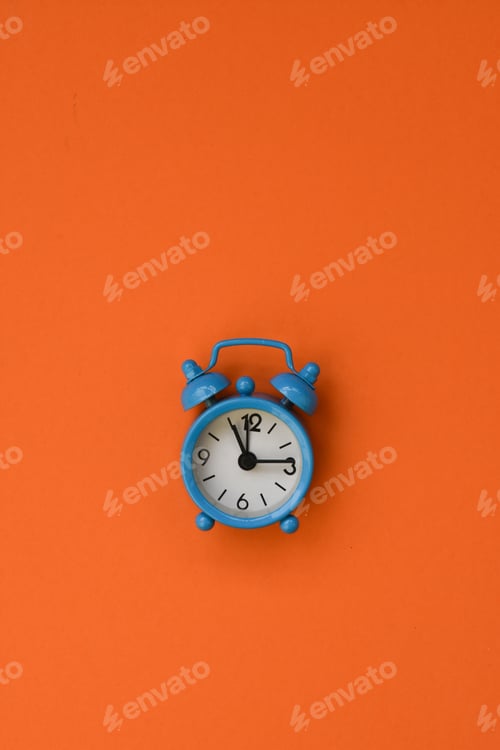 Preview: Blue alarm clock on orange background.Minimal flat lay concept.