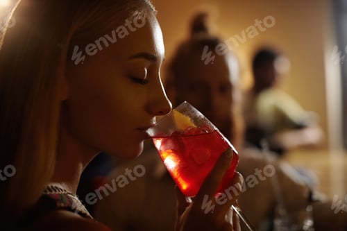 Preview: Close-up profile of glamorous blonde girl enjoying fresh fruit drink, sitting at bar counter next to