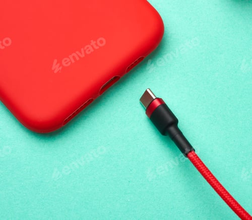 Preview: Red smartphone and cable in textile braid on a green background