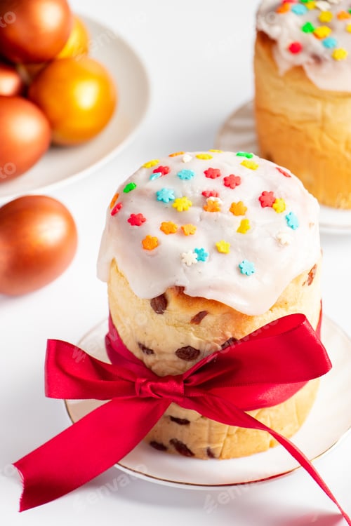 Preview: Easter cake panettone with sweet icing and golden eggs on white plate.