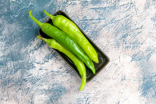 Preview: top view green hot peppers on black plate on blue-white background with copy space