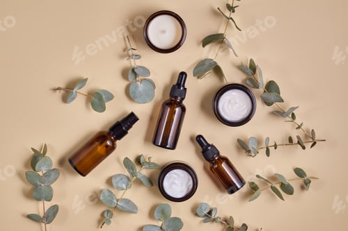 Preview: Set of beauty products in amber glass bottles and jars on beige background with eucalyptus leaves.