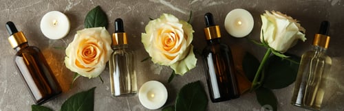Preview: Bottles with rose essential oil, roses and candles on gray textured background