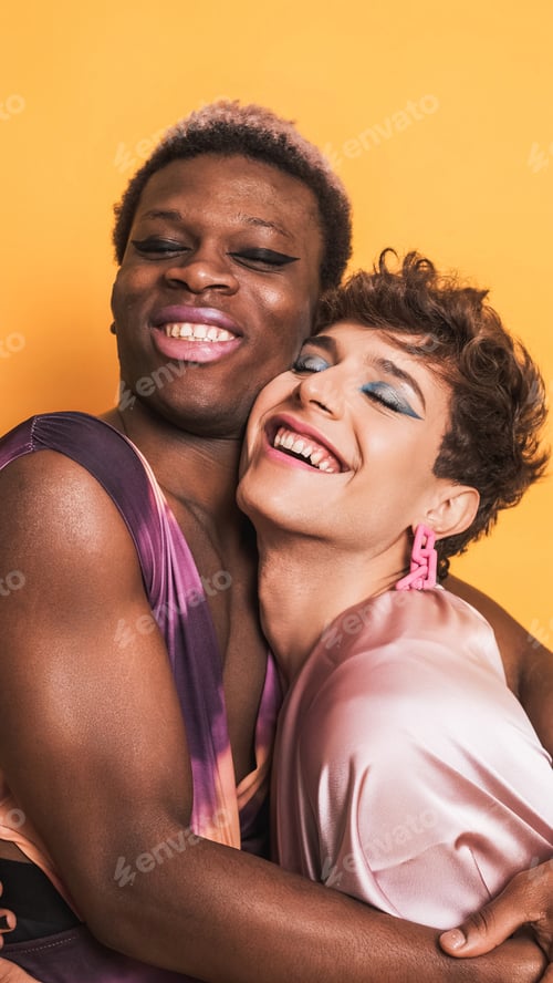 Preview: Stylish drag couple in make up and fashion clothes embracing and smiling on yellow