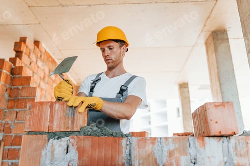 Preview: Working by using bricks. Young man in uniform at construction at daytime