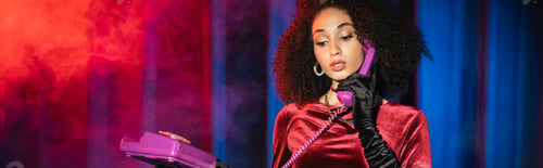 Preview: Elegant african american woman in velvet glove talking on telephone on red background with blue