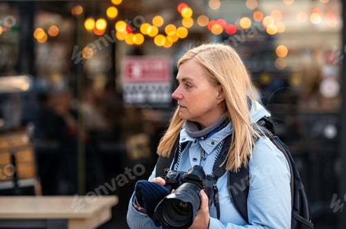 Preview: blonde middle-aged female with a camera in the evening on the city streets, lifestyle concept