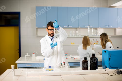 Preview: Young researcher in protective workwear standing in the laboratory and analyzing flask with liquid