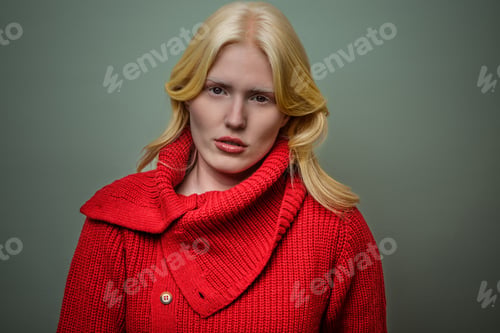 Preview: Blonde woman in red sweater poses against green background