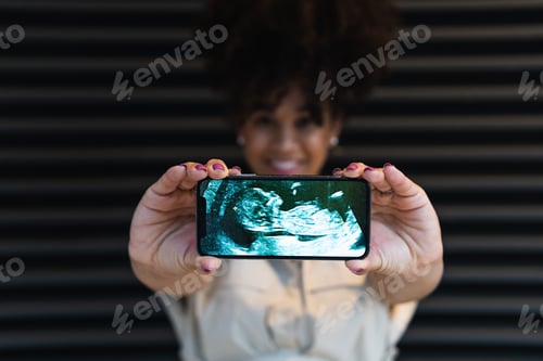 Preview: Smiling black woman showing smartphone screen with baby ultrasound