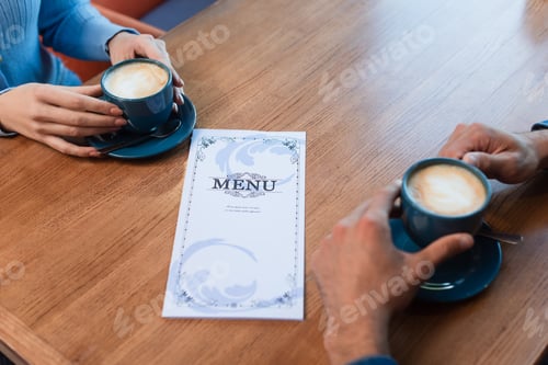 Preview: partial view of couple near coffee cups and menu on table