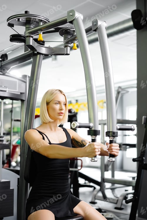 Preview: Woman who using simulator for raising and spreading hands for pumping group of muscles in gym