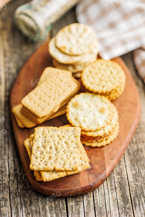 Preview: A stack of crackers neatly arranged on cutting board on wooden tabletop.