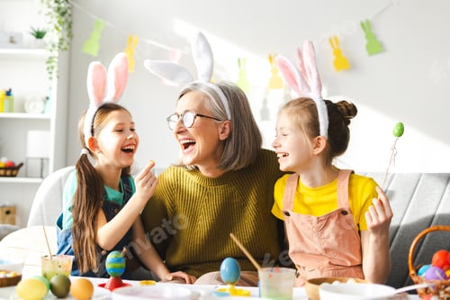 Preview: Happy family painting easter eggs together at home, little girls and grandmother in cozy living room