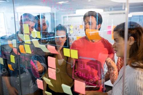 Preview: Creative business team looking at sticky notes on glass window