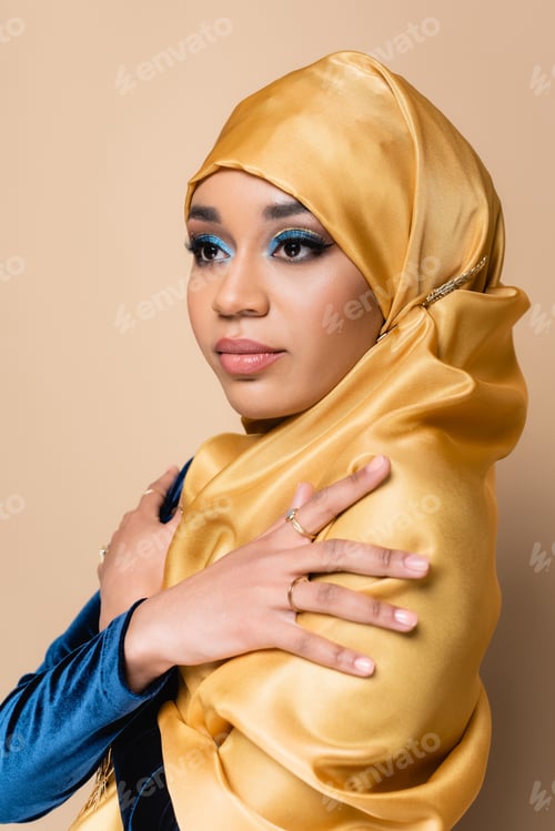 Preview: pretty muslim woman in yellow hijab posing with crossed arms isolated on beige