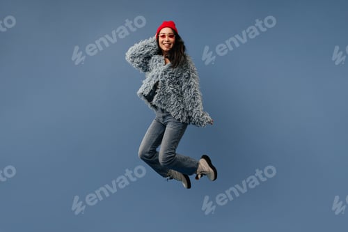 Preview: Charming long dark haired lady with red cap and sunglasses in modern cool blue outfit and boots jum
