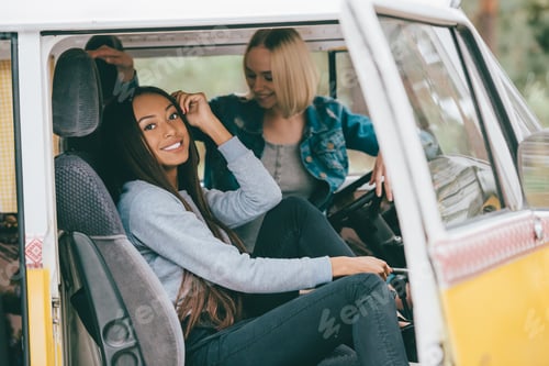 Preview: smiling multiethnic girls sitting in retro minivan