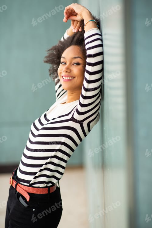 Preview: Portrait of happy young black woman leaning to wall
