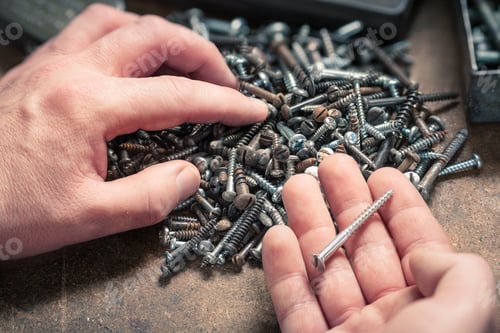 Preview: Pair of hands, one screw standing out from pile of different sized screws