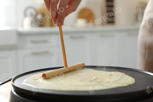 Preview: Woman cooking delicious crepe on electrical pancake maker in kitchen, closeup