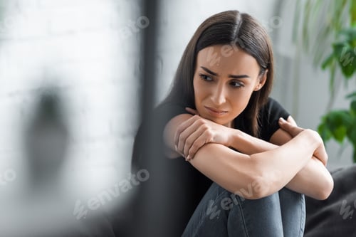 Preview: selective focus of crying young woman suffering from depression while sitting with crossed arms and