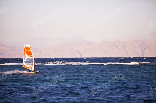 Preview: Sportman windsurfer on the sea surface against mountains at sunset time