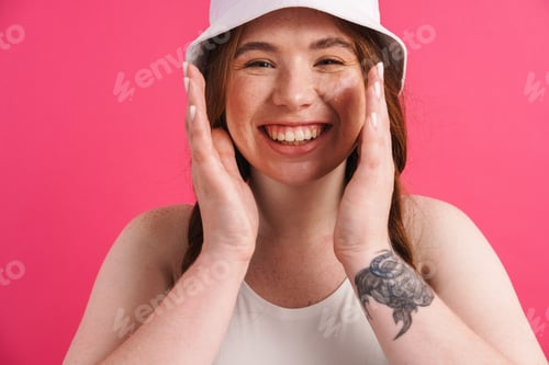Preview: Young ginger woman with tattoo smiling and gesturing at camera