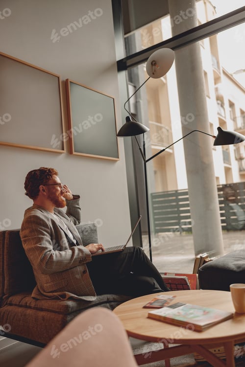 Preview: Smiling male sales manager in eyeglasses working on laptop sitting in office during working day