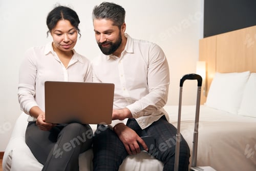 Preview: Young couple seated in hotel room looking at computer monitor