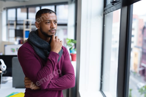 Preview: Mixed race businessman in thought looking through window in creative office