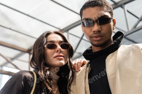 Preview: portrait of stylish interracial couple in trendy sunglasses looking at camera