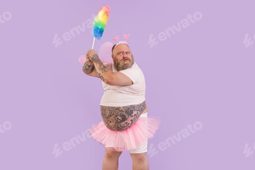 Preview: Bellicose actor man with overweight in fairy suit holds dust brush on purple background