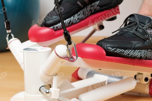 Preview: Close up mans feet in sneakers training on the twist stepper with digital display and gum expanders