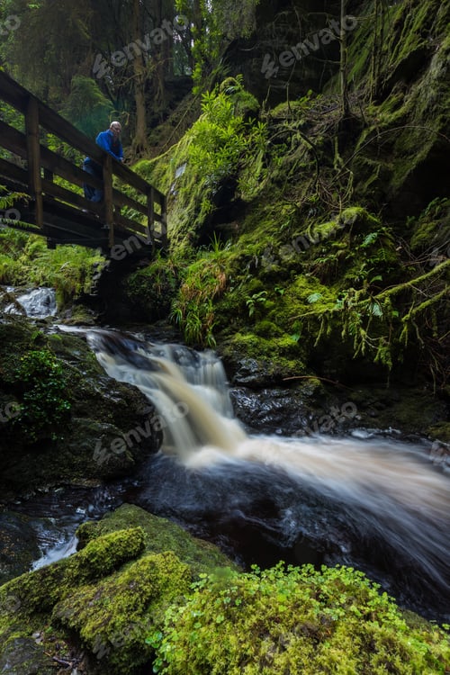 Preview: Man standing on a bridge over a waterfall