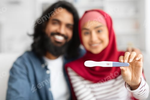 Preview: Happy muslim couple showing positive pregnancy test at camera