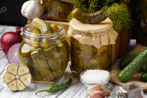 Preview: Pickled cucumbers in glass jars, spices, vegetables for preparation of pickles on wooden background.