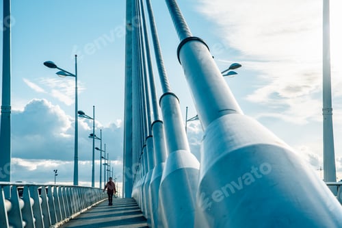 Preview: Person walks on an industrial bridge with large pylons and cable ties.