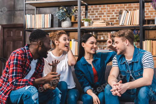 Preview: cheerful young multiethnic friends talking while sitting together on sofa