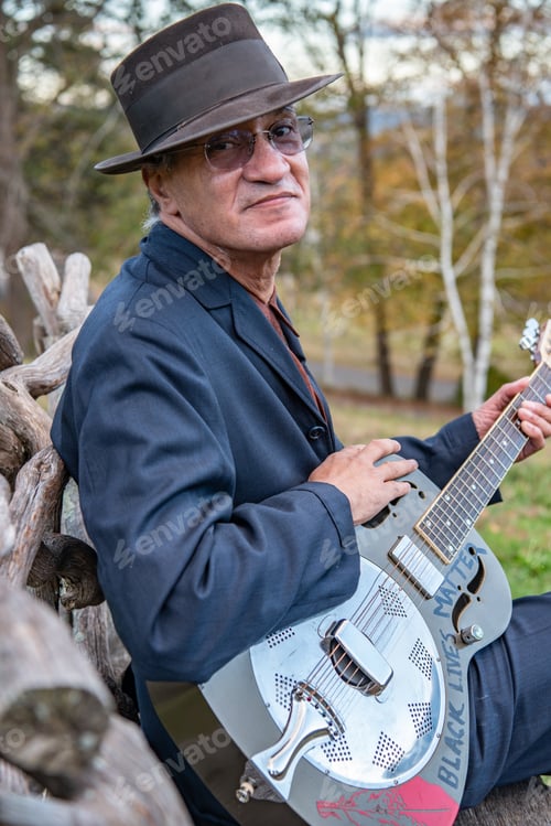 Preview: A seasoned musician plays the blues on a park bench in the fall.