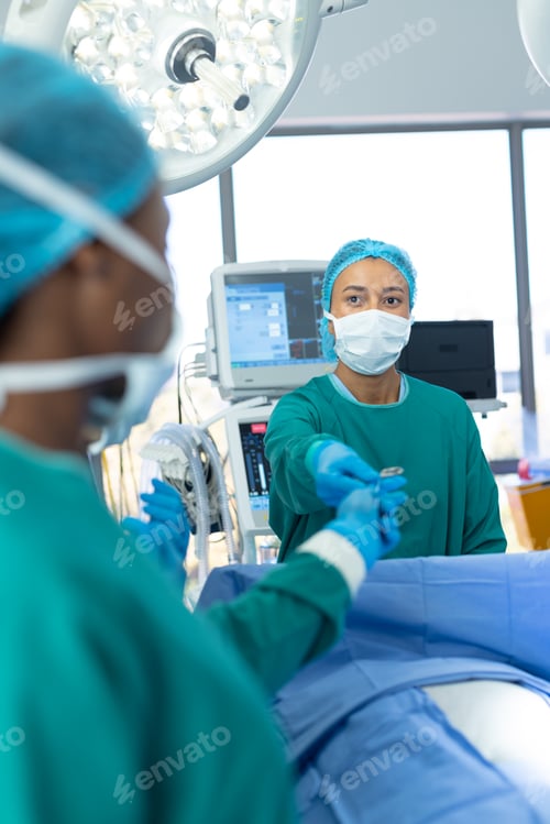 Preview: Vertical of biracial female surgeon passing tool in theatre during operation, with copy space