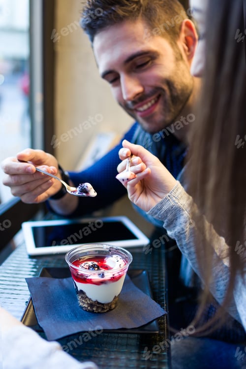 Preview: Beautiful young couple eating iogurt in restaurant.