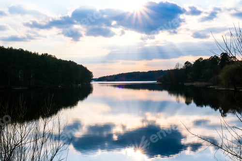 Visualização: Vista panorâmica do lago calmo ao pôr do sol. Raios solares do tempo do rio. Nuvens. Efeito espelho. Fundo da natureza