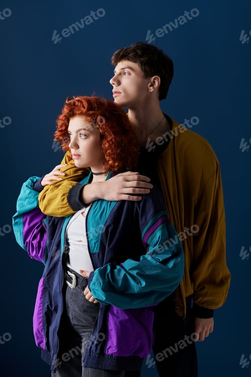 Preview: alluring loving couple in stylish casual clothing hugging and looking away on blue backdrop