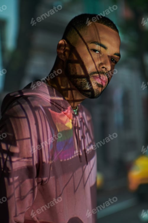Preview: handsome man with beard in pink hoodie looking at camera in projector lights, fashion concept